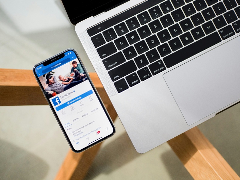 Facebook on a smartphone next to laptop on a glass table with oak legs